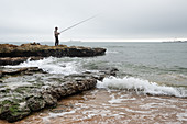 Angler on rocks at the beach Praia do Tamariz, Cascais, Portugal