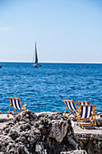 Liegestühle und Segelboot an der Küste, Insel Capri, Golf von Neapel, Italien