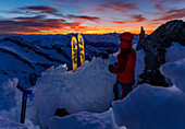 Junge Frau genießt die Aussicht über die Hochgebirgslandschaft im Abendlicht von ihrem winterlichen Biwakplatz aus, Valser Tal, Tirol, Österreich