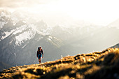 Junge blonde Frau in kurzer Hose beim Wandern in herrlichen warmen Gegenlicht  mit verschneiten Bergen im Hintergrund, Hinterriss, Karwendel, Tirol, Österreich