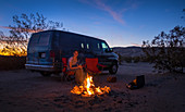 Woman by the campfire and van on the sand dunes of Kelso in the Mojave National Park at sunset