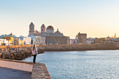 Frau blickt von der Uferpromenade auf die Kathedrale Santa Cruz und den Ozean, Cádiz, Andalusien, Spanien, Europa