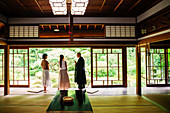 Buddhist priest and two Japanese women standing in Buddhist temple.