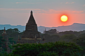Sunset over distant mountains with stupa of temple in the foreground, Bagan, Myanmar.
