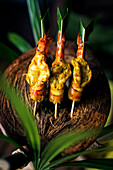 High angle close up of charcoal-grilled prawn satay on a coconut shell.