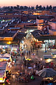 Menschenmassen von Einheimischen und Touristen, die bei Sonnenuntergang zwischen den Geschäften und Ständen im Djemaa el Fna spazieren gehen, Marrakesch, Marokko, Nordafrika, Afrika