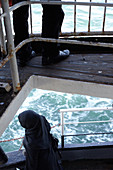 Male legs and the figure of a Muslim woman on the railing of the ferry from the European part to the Asian part of the city of Istanbul, Turkey