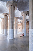 Woman sits in Sala Hipostila on stone columns in Park Guell, Barcelona
