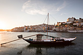 Traditionelle Schiffe auf dem Fluss Douro in Porto bei Sonnenuntergang, Portugal\n