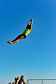 Eine junge Frau wird von ihren Freunden hoch in die Luft geworfen und übt Akrobatik am Santa Monica Beach, Kalifornien, USA