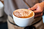 Hand hält eine Tasse Cappuccino