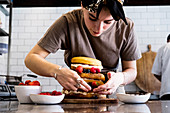 A cook working in a commercial kitchen assembling a layered sponge cake with fresh fruit.