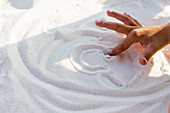 young boys hand making a design in sand