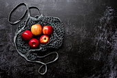 High angle close up of red apples in grey net bag on black background.