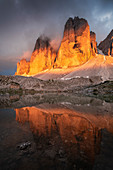 Dramatisches Alpenglühen der Drei Zinnen mit Spiegelung in Bergsee bei Sonnenuntergang, Südtirol