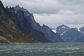 Prins Christian Sund in South Greenland; Passage on the southern tip between East and West Greenland; rugged mountains with steep, rocky slopes; in places snow fields and foothills of a glacier; bad weather and low hanging rain clouds