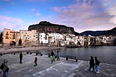Evening on the beach of Cefalu with its old waterfront houses under the rock, north coast, Sicily, Italy