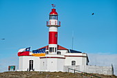 Der historische rot-weiße Leuchtturm steht auf einem Hügel und dominiert die Silhouette der Insel, Isla Magdalena, Magallanes y de la Antartica Chilena, Patagonien, Chile, Südamerika