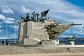 Fußgänger stehen in der Nähe eines Denkmals in Form eines Schiffsbogens (Goleta Ancud) an der Strandpromenade, Punta Arenas, Magallanes y de la Antartica Chilena, Patagonien, Chile, Südamerika