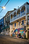 Two young women examine street art on a historic building in the streets of Valparaiso, Chile, South America