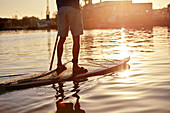 Man standing on paddleboard on river at dawn, shot from behind
