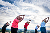 Group of women taking part in a yoga class on a hillside.