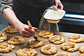 Baker with a pastry brush adding glaze to a tray of  cinnamon buns ready for the oven.