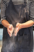 Artisan baker in apron patting her hands with flour.