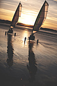 Zwei Strandsegler fahren bei Sonnenuntergang am Sandstrand entlang