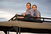 Mother and teenage daughter on top of safari vehicle looking into the distance.