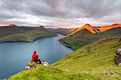 Hiker is admiring the fjord at dusk, Funningur, Eysturoy island, Faroe Islands, Denmark