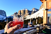 Campari Soda on the pass road of the Pordoi Joch, Campari, drink, mountains, hut, apresski, hand holds drink, Sellastock, Dolomites, Trentino in winter, Italy