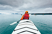 A person paddling in a double sea kayak on calm water off the coast of Alaska.