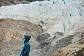 A young woman standing at the end of a glacier on a rocky shoreline in Alaska.