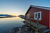 Typisches rotes Haus eines Fischers am Meer in der Morgendämmerung im Winter, Svolvaer, Nordland, Region Nordnorwegen, Norwegen