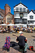 Vereinigtes Königreich, Devon, Exeter, Straßengitarrist spielt vor einer überfüllten Caféterrasse am Fuße historischer Häuser