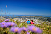 Man and woman while hiking sit in meadow and look into the distance, Picos de Europa, Picos de Europa National Park, Cantabrian Mountains, Asturias, Spain