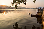 Baden am frühen Morgen im Pichhola-See mit Blick auf City Palace, Udaipur, Rajasthan, Indien