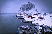 Dämmerung über dem eisigen Meer, das das mit Schnee bedeckte Fischerdorf Hamnoy, Nordland, Lofoten-Inseln, Norwegen umgibt