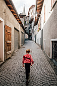 Rear view of boy walking down a narrow lane in Bormio, Lombardy, Italy.