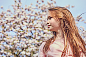 Porträt des brünetten Mädchens, das draußen steht, Baum mit rosa Blüten im Hintergrund.