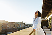 Woman enjoying sun on hotel balcony, Florence, Toscana, Italy