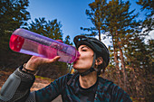 Weiblicher Mountainbiker, der von der Wasserflasche in einem Wald trinkt