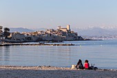 France, Alpes-Maritimes, Antibes, beach of Ponteil, old Antibes and his ramparts Vauban, both saracen towers of the castle Grimaldi with in background the Alps of the South covered with snow