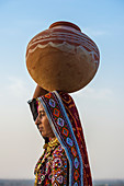 Ahir Frau in traditionellem buntem Stoff, der Wasser in einem Tonkrug auf ihrem Kopf trägt, großer Rann der Kutch-Wüste, Gujarat, Indien, Asien