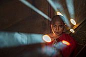 Novice Buddhist monk praying with shafts of light, Bagan, Myanmar (Burma), Asia