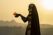 Ahir Woman in traditional colorful cloth pouring water at sunset, Great Rann of Kutch Desert, Gujarat, India, Asia