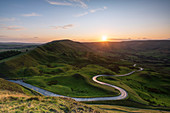 Lange und kurvenreiche Landstraße, die durch grüne Hügel im Peak District mit Rushup Edge, Nationalpark Peak District, Derbyshire, England, Vereinigtes Königreich, Europa führt