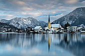 View over the wintry Tegernsee to the village of Rottach-Egern with the church Sankt Laurentius, Bavaria, Germany.