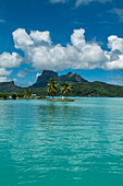 Two palm trees and a tiki sculpture on a small island at the entrance to Bora Bora Airport (BOB) harbor with Mount Otemanu in the distance, Bora Bora, Leeward Islands, French Polynesia, South Pacific